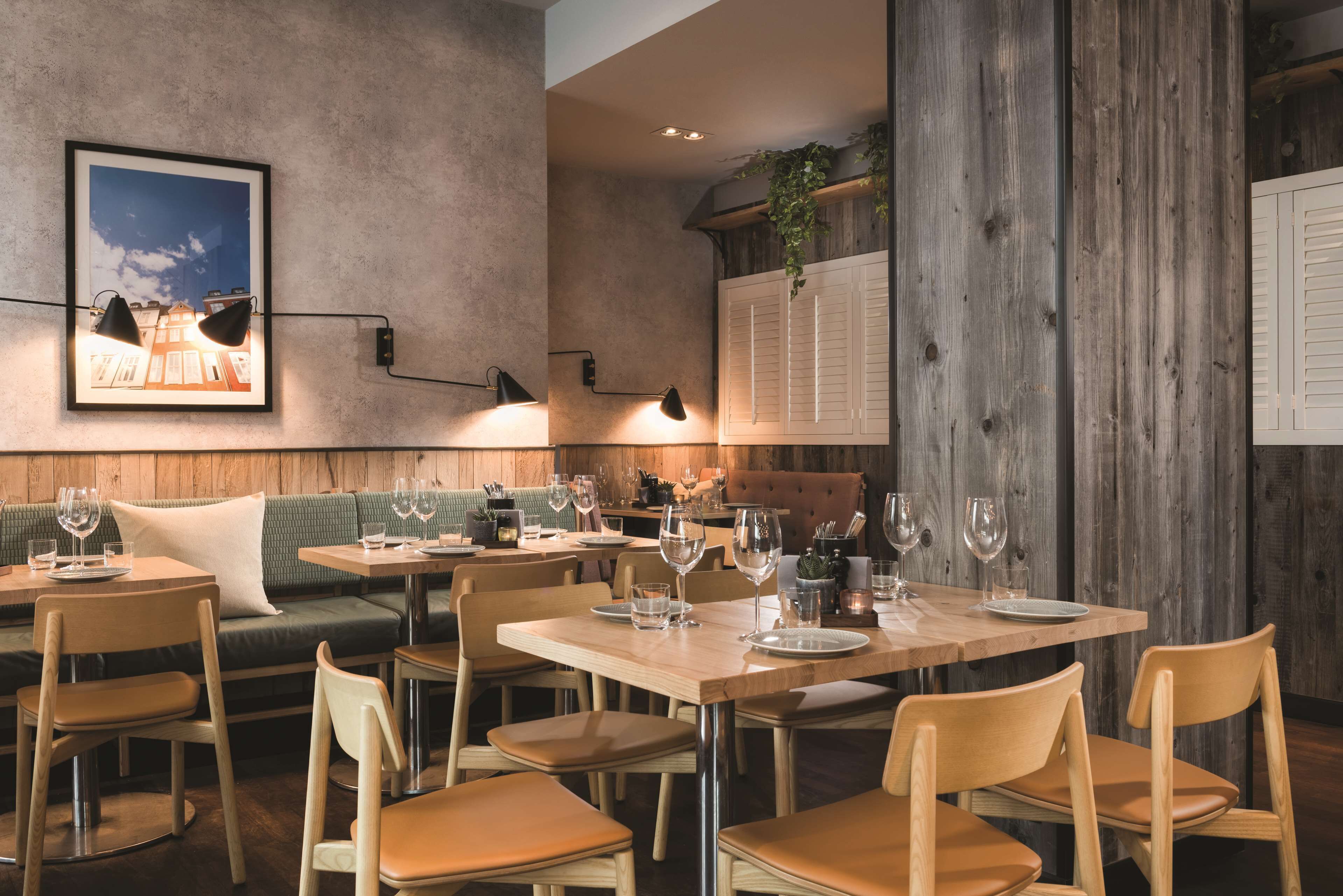Interior de restaurante con mesas y sillas de madera, un banco con cojín verde y un cuadro en la pared.