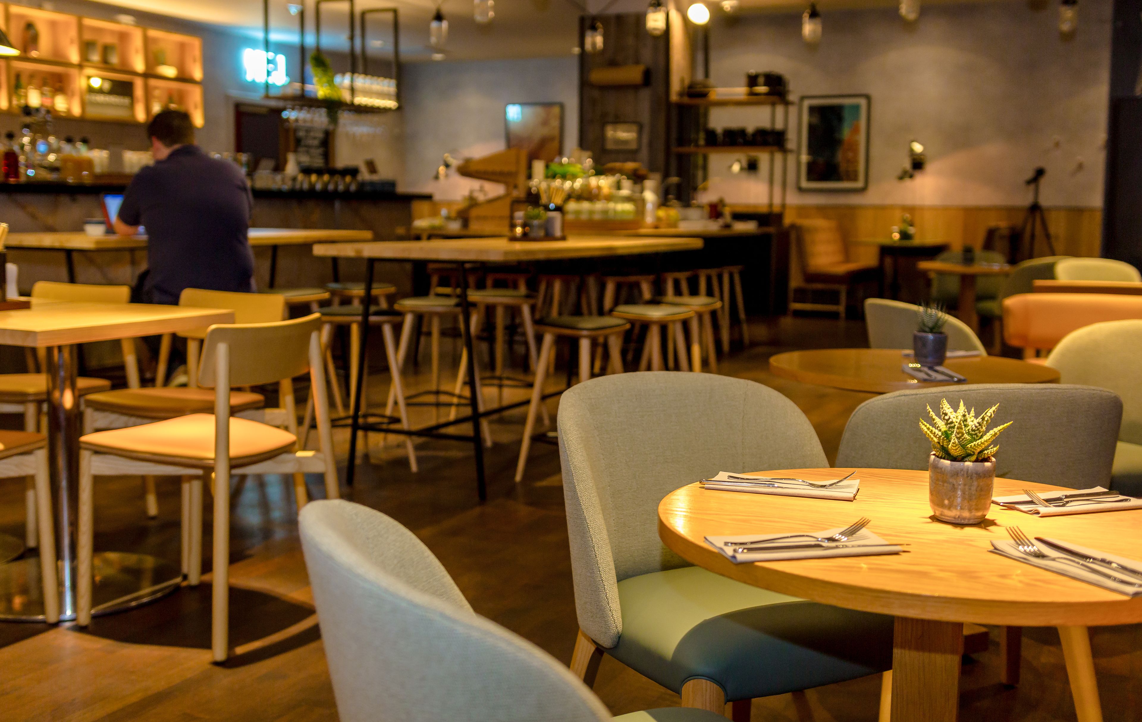 A restaurant with round tables, chairs, and a bar area in the background.