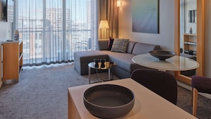 Habitación de hotel moderna con sofá, una pequeña mesa redonda, un espejo grande y vistas a la ciudad a través de cortinas translúcidas.