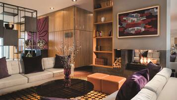 A modern living room with a sofa, ottoman, coffee table, and a fireplace.