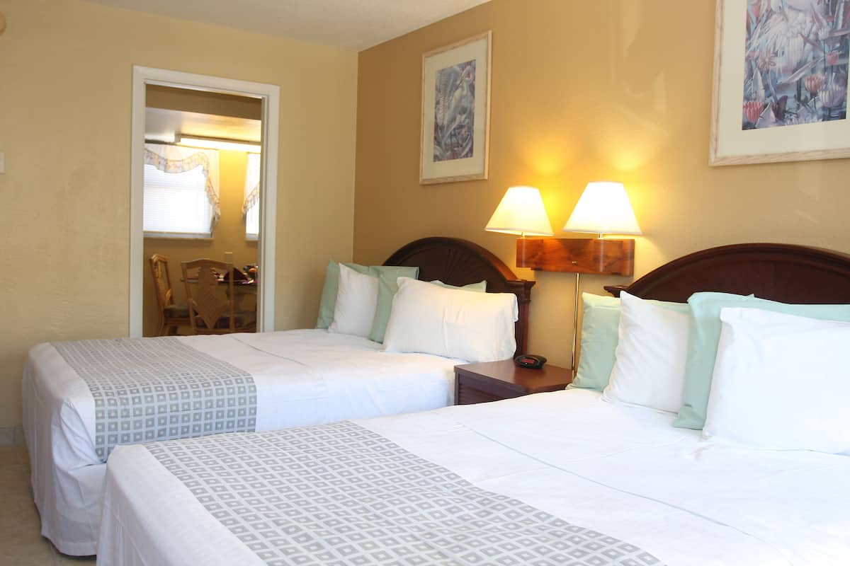A hotel room with two beds, a nightstand, a lamp, and a painting on the wall.