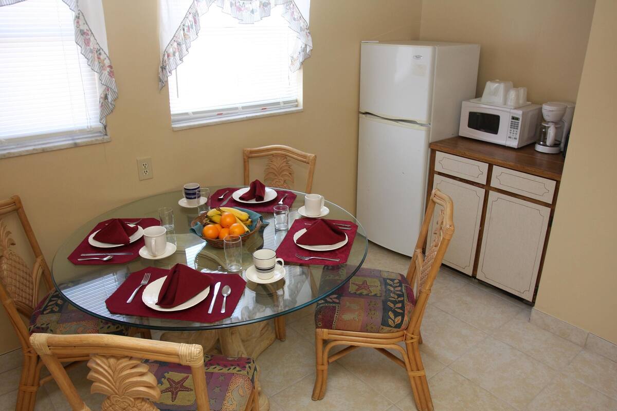 A dining area with a glass table, wicker chairs, and a white refrigerator.
