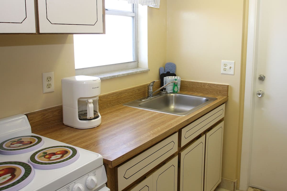 A compact kitchen with a stove, a coffee maker, a sink, and wooden cabinets.