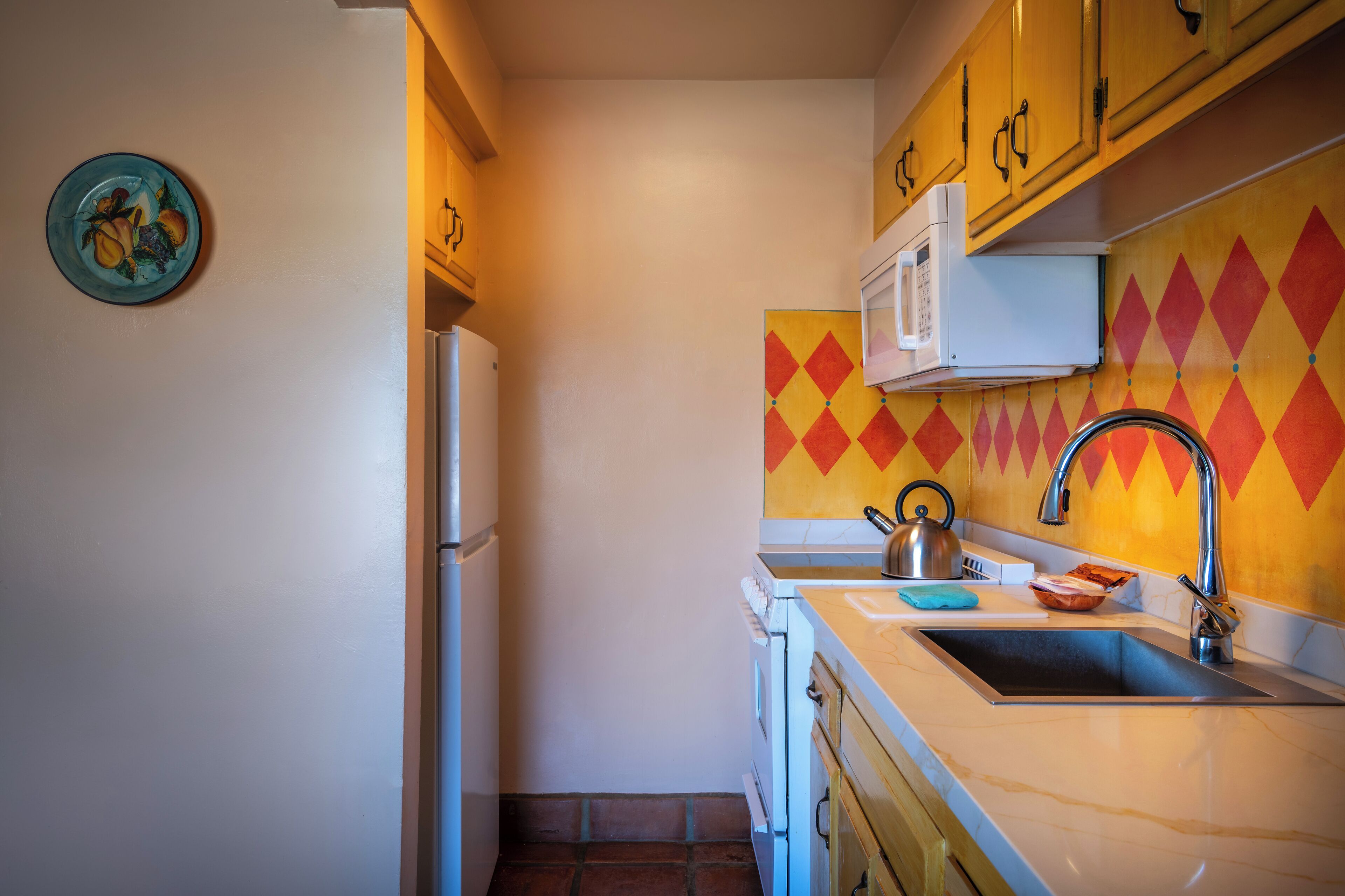 Una cocina compacta con microondas, pileta y un detalle decorativo en la pared.