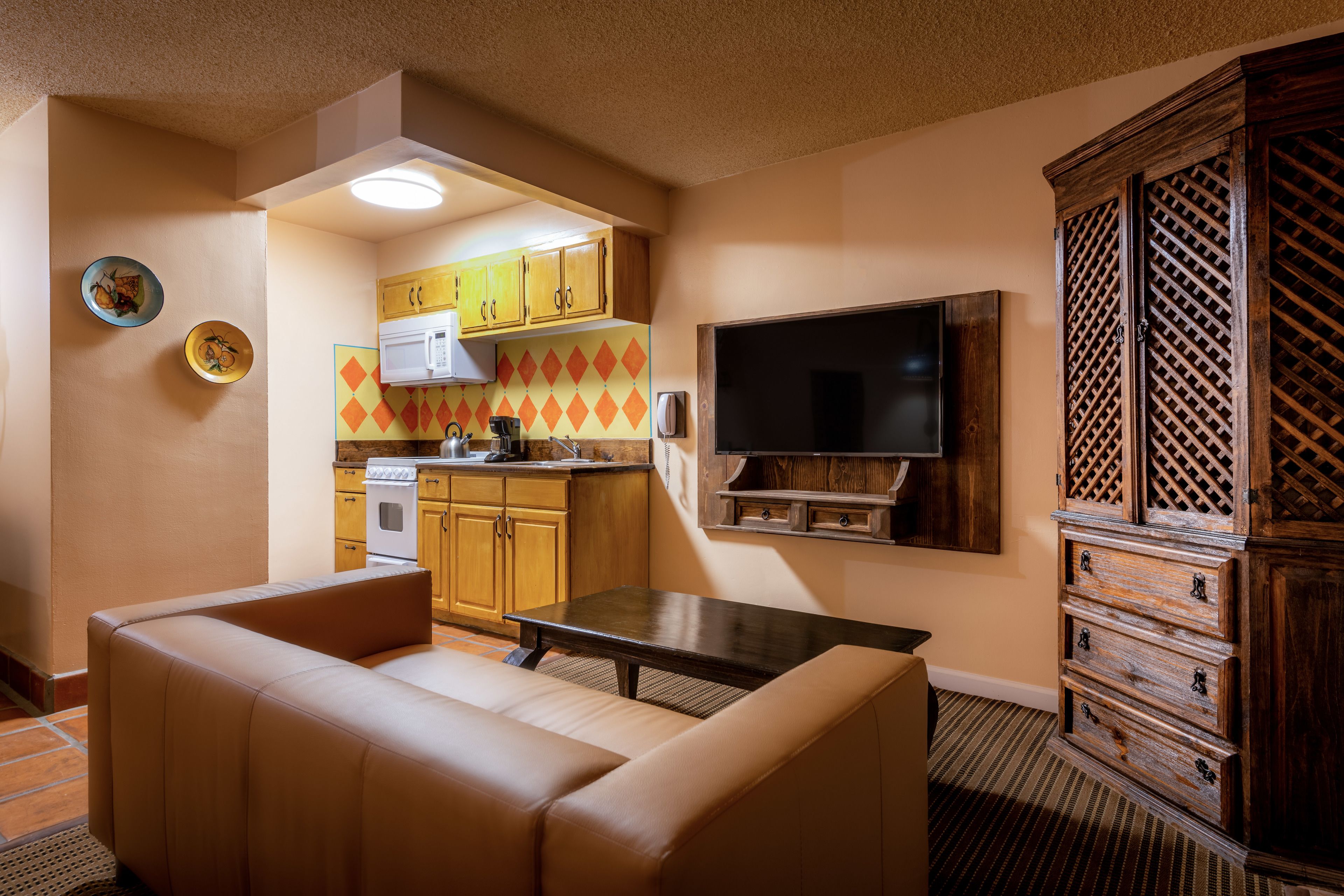 Een ruimtelijk ingerichte leefruimte met kitchenette, een bank, een televisie en een houten kast.