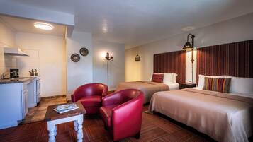 Habitación de hotel con kitchenette, dos camas, una silla roja, una mesita y piso con diseño.