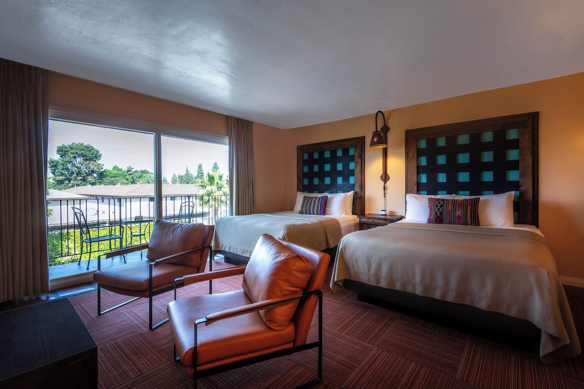 A hotel room with two beds, a sofa, a desk, and a balcony with a view of greenery.