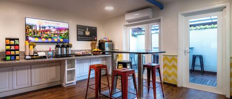 A kitchen with wooden flooring, a bar area with stools, a television displaying a hotel, and a door leading to an outdoor area.