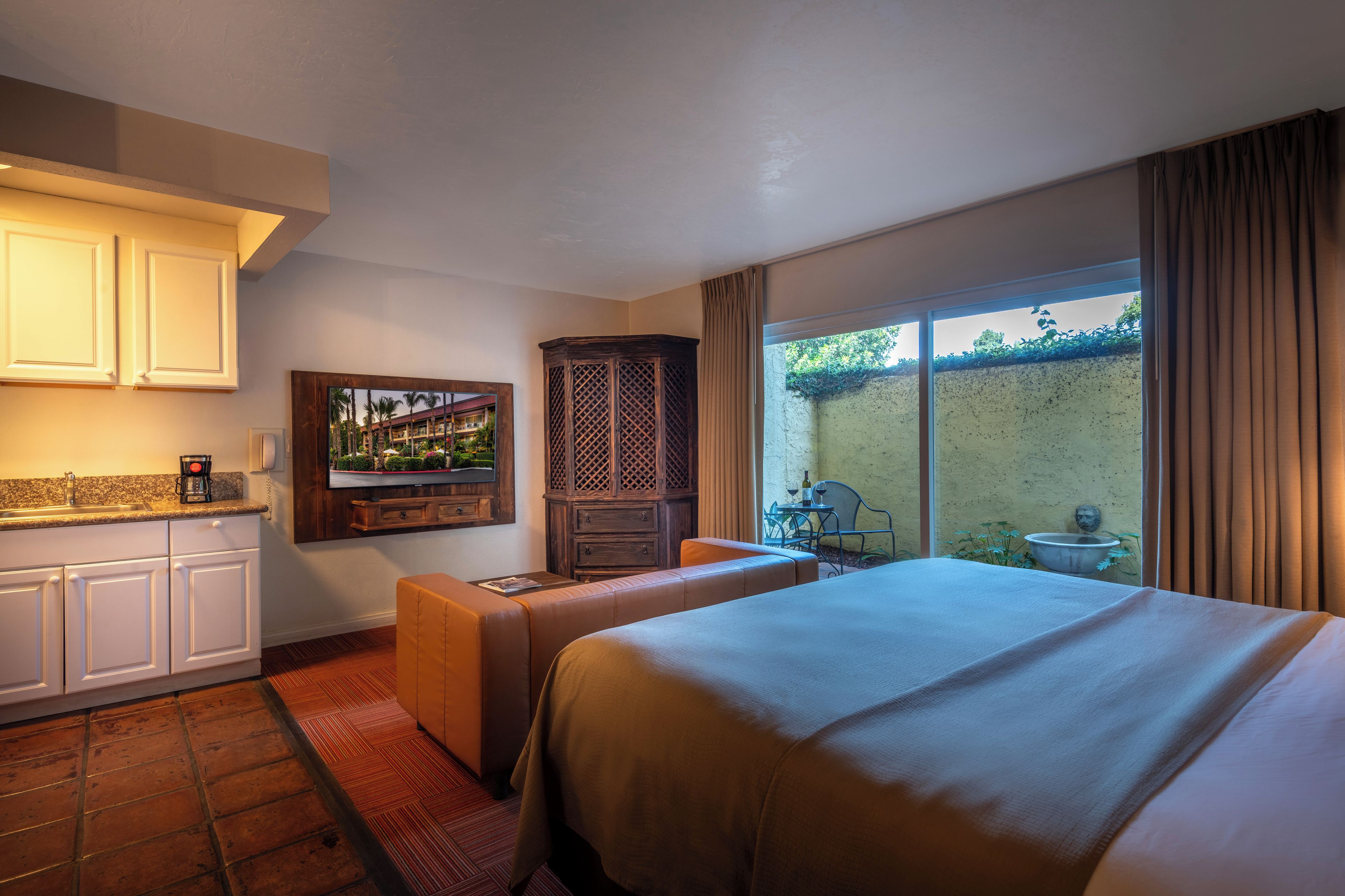 A hotel room with a bed, a seating area, a kitchen with a coffee maker, and a view of the outdoors.