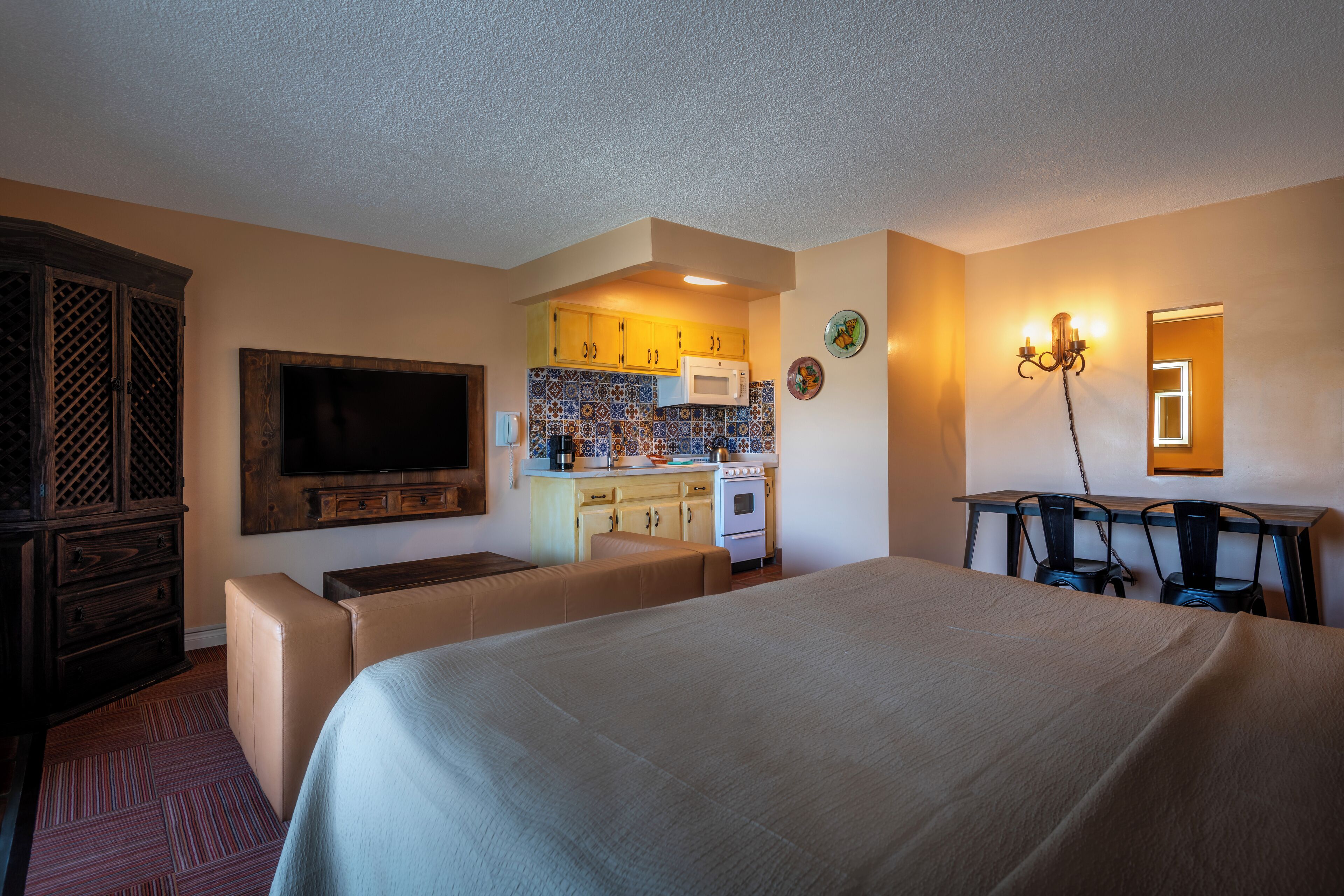 A hotel room with a large bed, a television, a kitchenette, and a dining area.