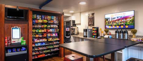 A hotel lobby with a snack bar, a television, and a coffee station.
