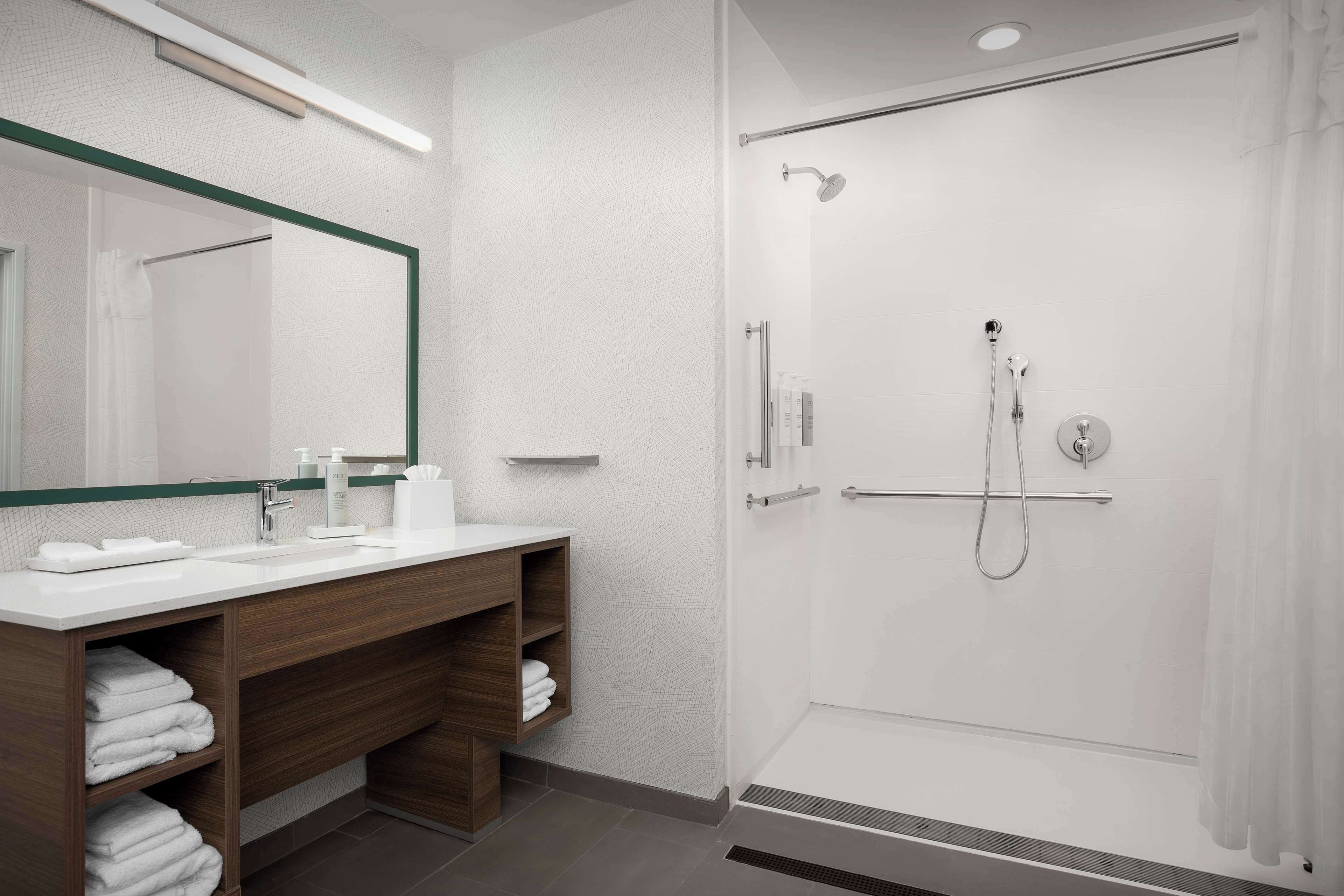 Un baño moderno con cabina de ducha acristalada, tocador de madera con espejo y toallas ordenadas.