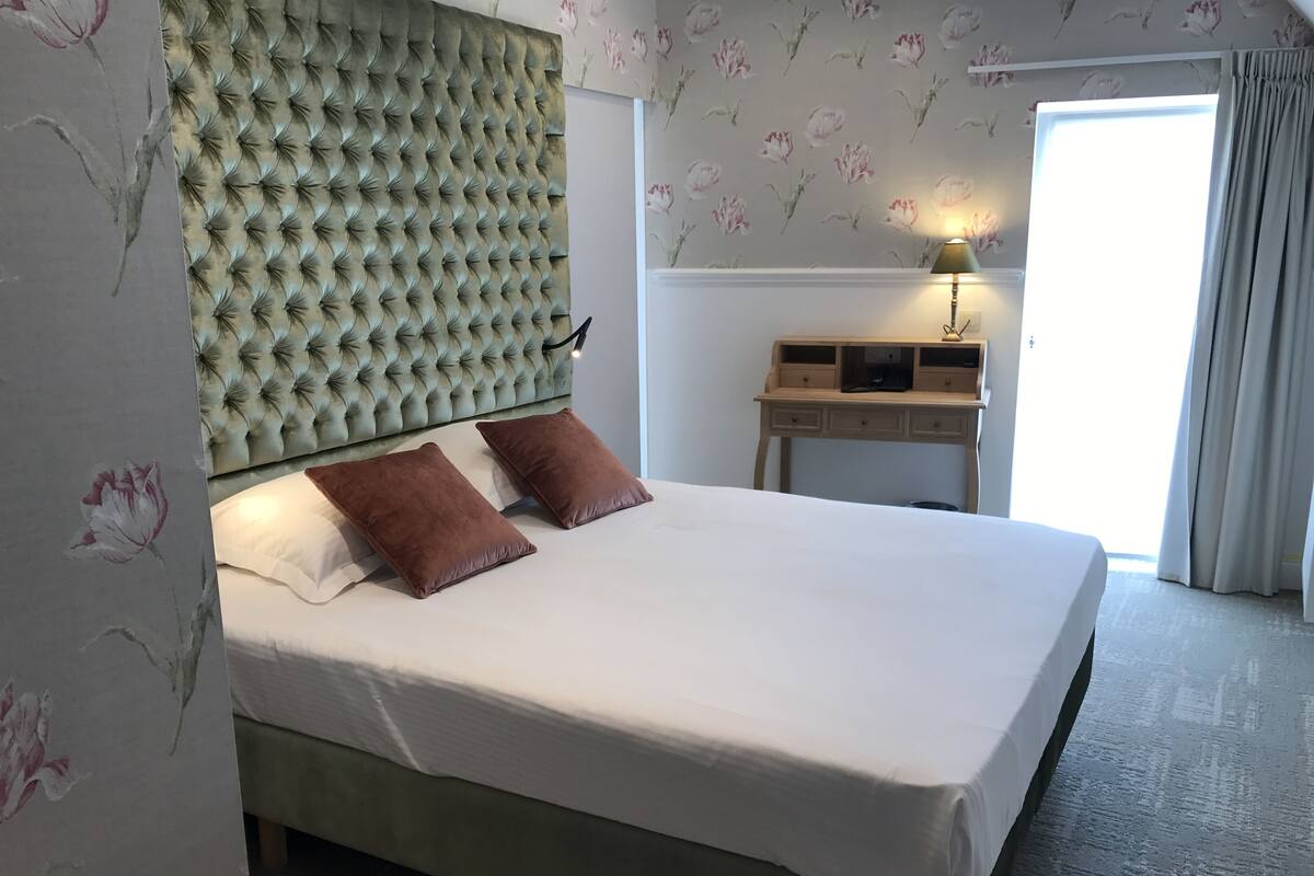 A neatly made bed with a tufted headboard, two pillows, and a bedside table with a lamp.