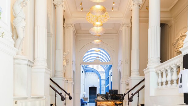 A grand lobby with marble floors, white columns, and blue armchairs. - Golden Tree Hotel (Bruges)