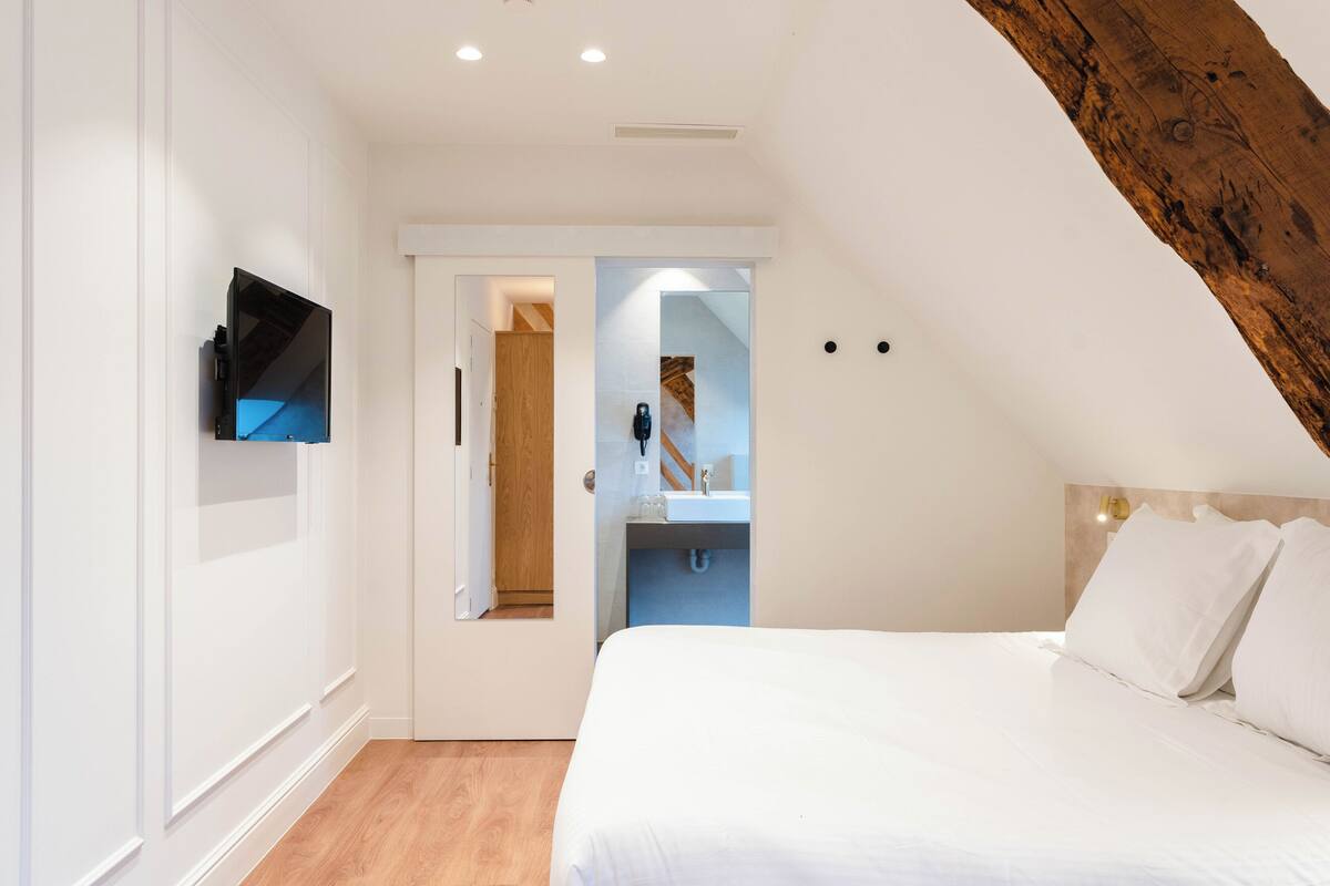A bedroom with a bed, a TV mounted on the wall, and a bathroom visible through an open door.