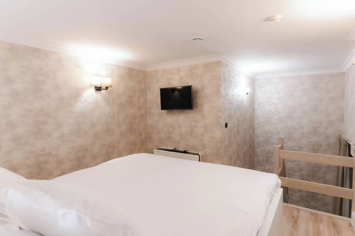 A bedroom with a bed, a flat-screen TV mounted on the wall, and a wooden headboard.