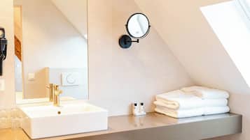 A modern bathroom with a large mirror, a white sink, a towel rack, and a toilet.