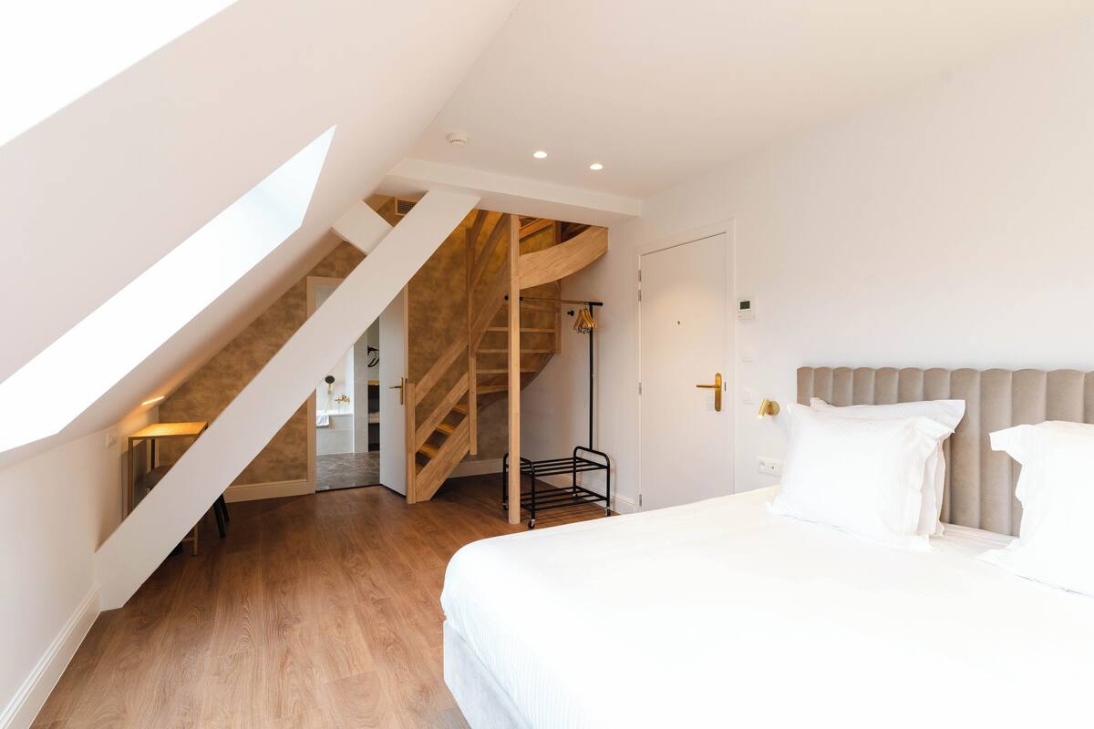 A bedroom with a bed, a wooden staircase, and a door.