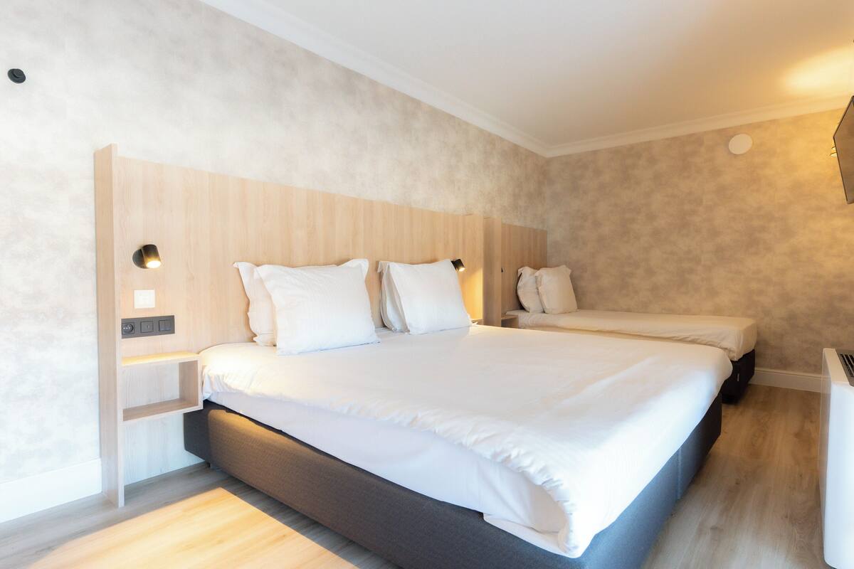 A modern hotel room with a large bed, a smaller bed, and a built-in bench.