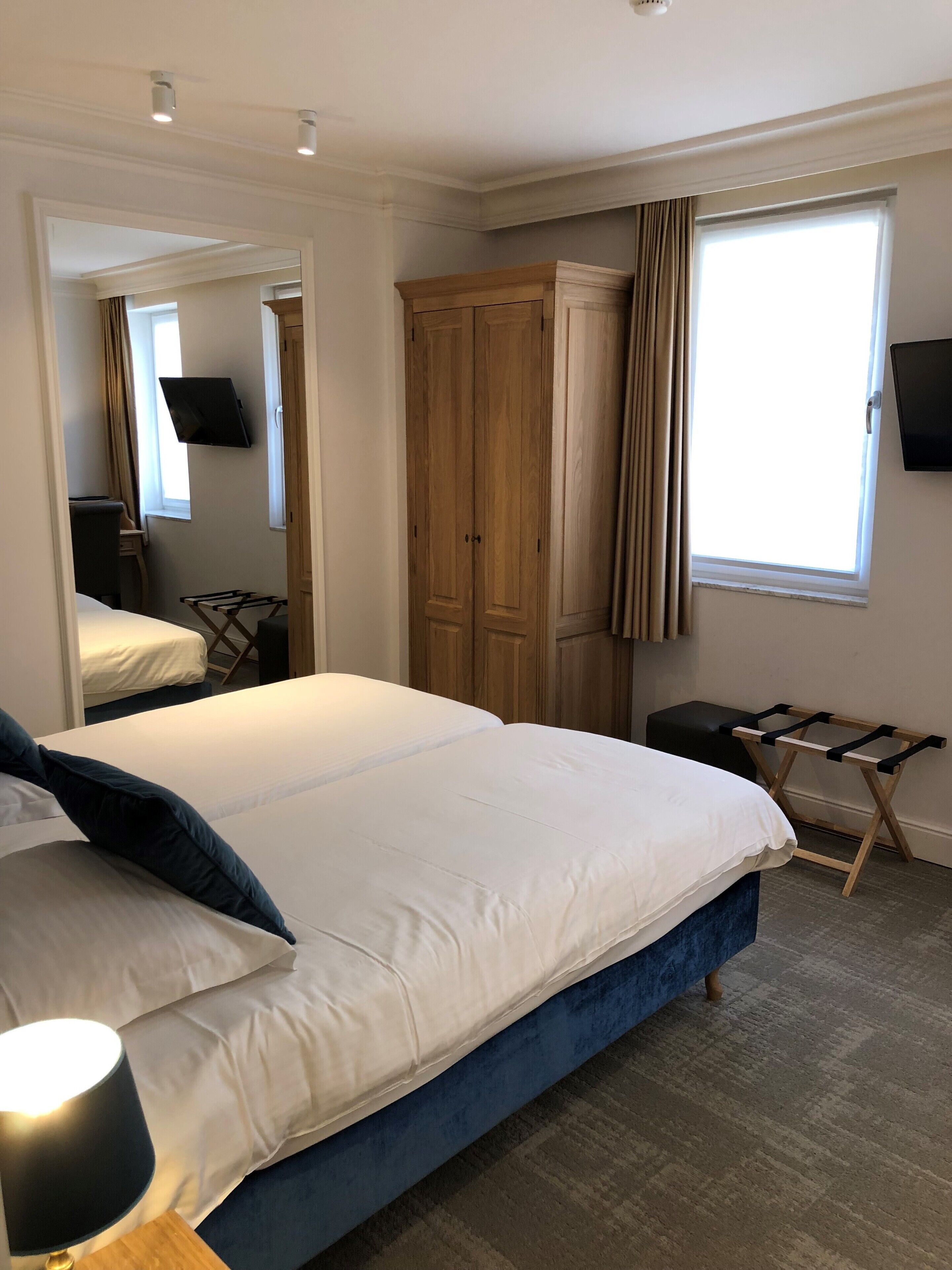 A hotel room with a large bed, a wardrobe, a television, and a window with curtains.