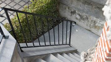 Un escalier en béton avec une rampe métallique, un petit arbuste et un mur en briques.