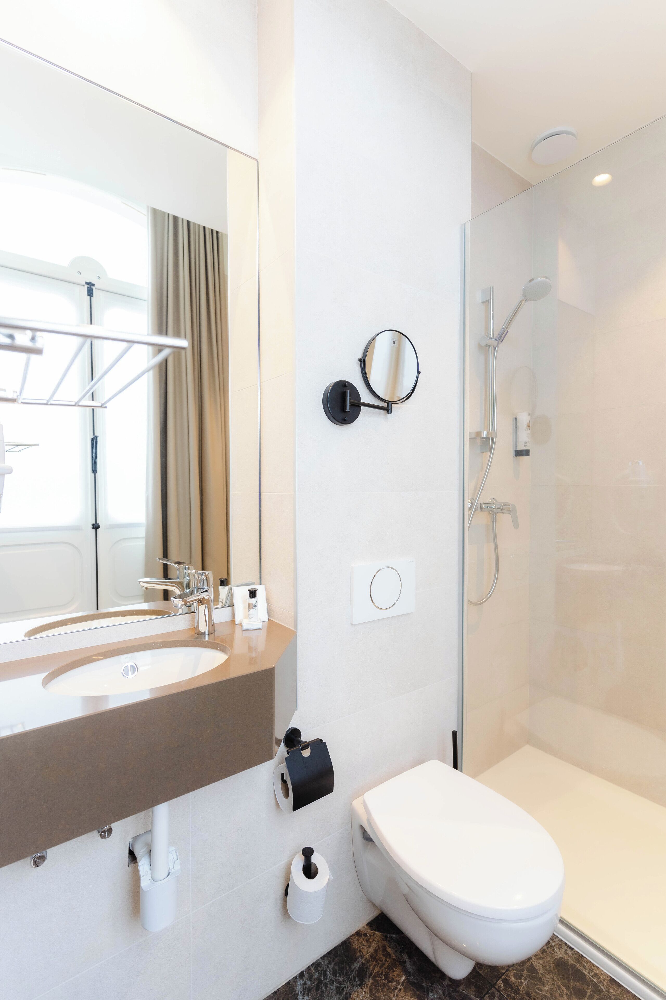 Ein modernes Badezimmer mit großem Spiegel, Waschbecken, Toilette und einer Duschkabine.