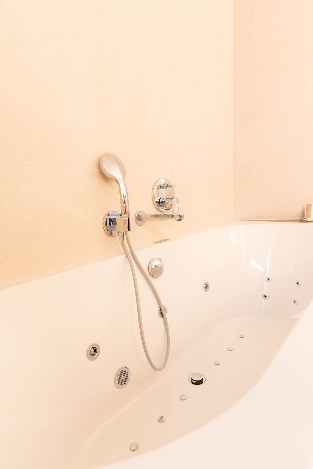 A modern bathtub with a handheld showerhead and a wall-mounted control.