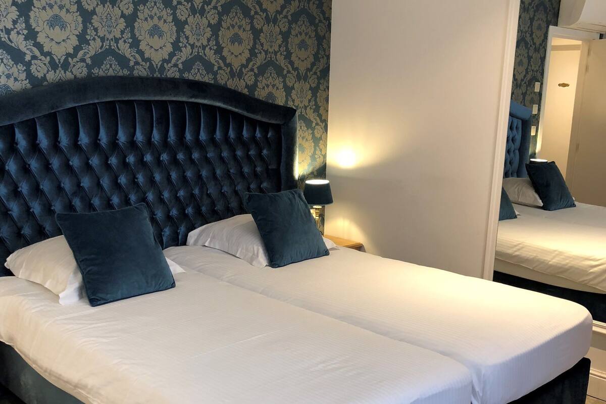 A double bed with a tufted headboard, two bedside tables with lamps, and a large mirror on the wall.