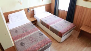 Habitación de hotel con dos camas individuales, cabeceros de madera, una mesita de noche pequeña y un ventanal con cortinas.
