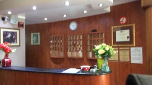 Un mostrador de recepción de madera con un reloj, diplomas enmarcados y un jarrón de flores.