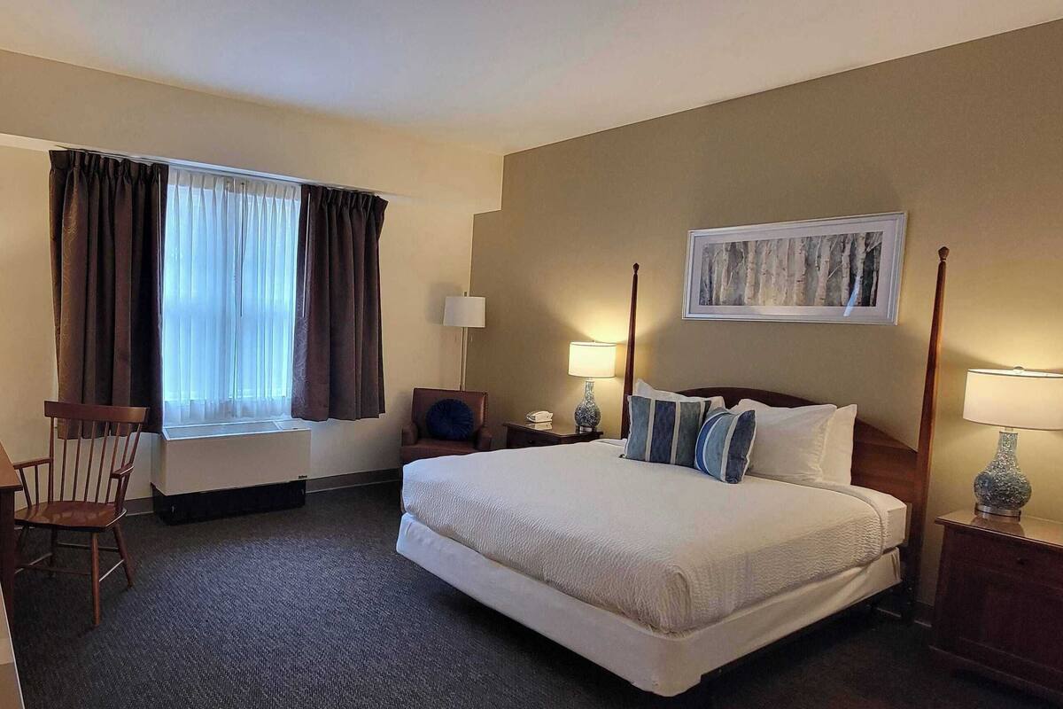 A hotel room with a bed, a desk, a chair, a TV, and a window with curtains.