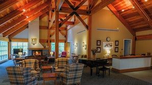 A spacious lobby with high ceilings, wooden beams, plaid armchairs, a piano, and a reception desk. - Warren Conference Center and Inn (Ashland)
