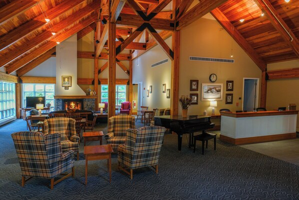 A spacious lobby with high ceilings, wooden beams, plaid armchairs, a piano, and a reception desk. - Warren Conference Center and Inn (Ashland)