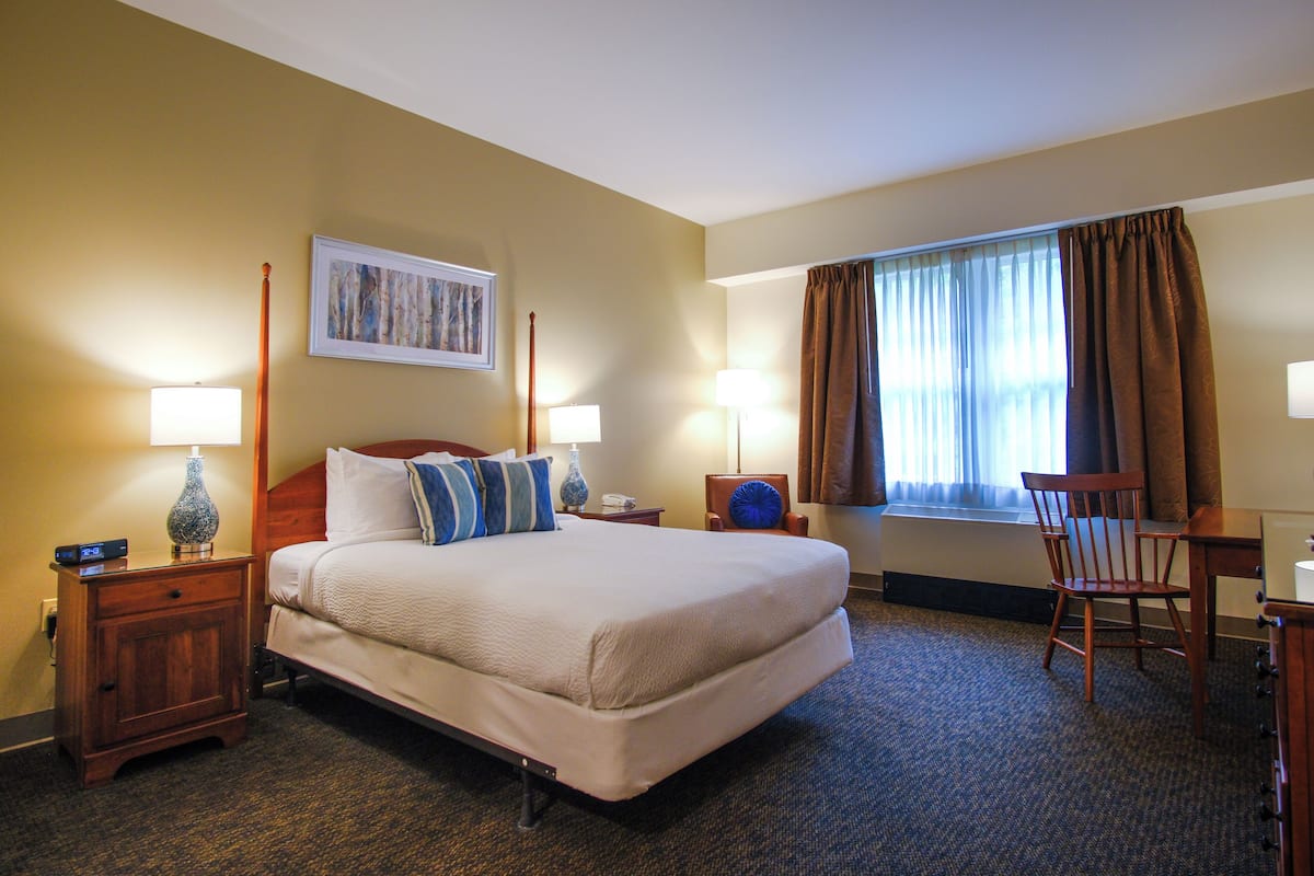 A hotel room with a large bed, two bedside tables with lamps, a chair, a desk, and a window with curtains.