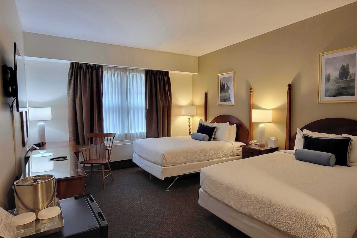 A hotel room with two beds, a desk, a chair, and a TV.