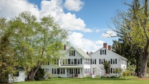 A large, two-story house with a wrap-around porch, surrounded by lush greenery and trees. - Warren Conference Center and Inn (Ashland)