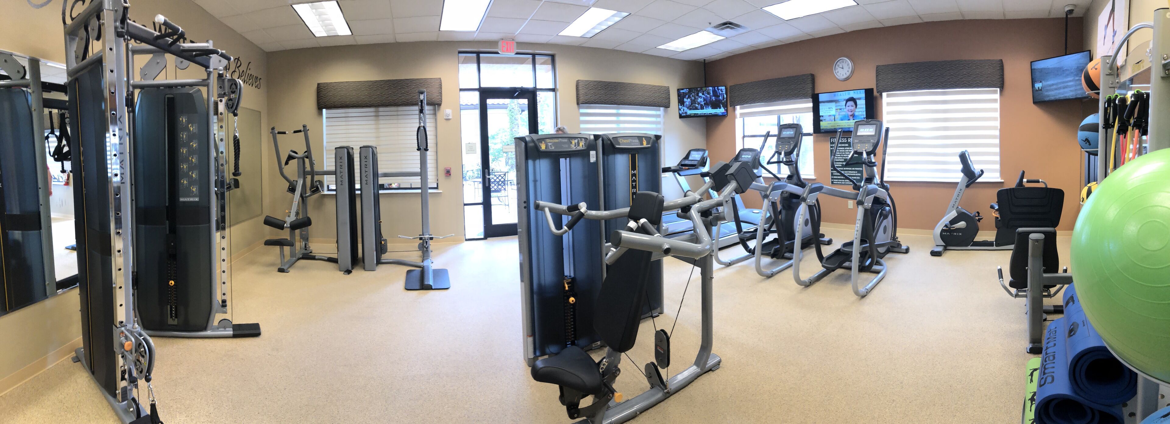 A gym with various exercise machines, a television, and a clock on the wall.