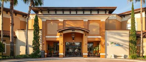 A hotel entrance with a covered entrance, palm trees, and a clear sky.