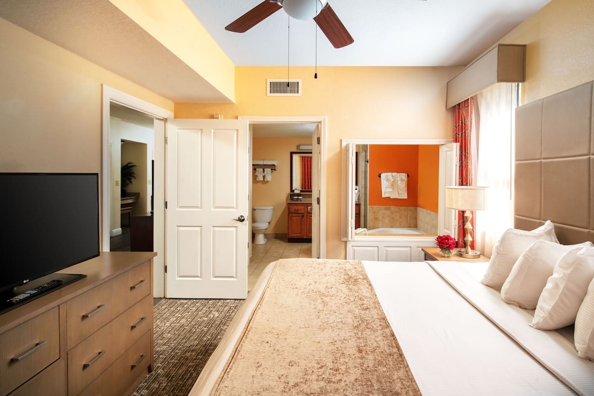 Una habitación de hotel con cama, televisión, armario, baño y ventilador de techo.