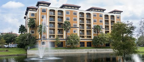 A multi-story hotel with balconies, a fountain, and a pond.
