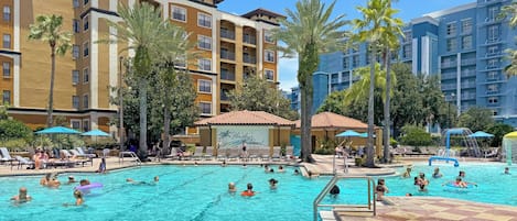 A swimming pool area with lounge chairs and umbrellas, surrounded by multi-story buildings with balconies.