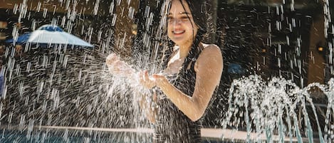 Una persona en traje de baño de pie en una piscina con chorros de agua apuntando hacia arriba.