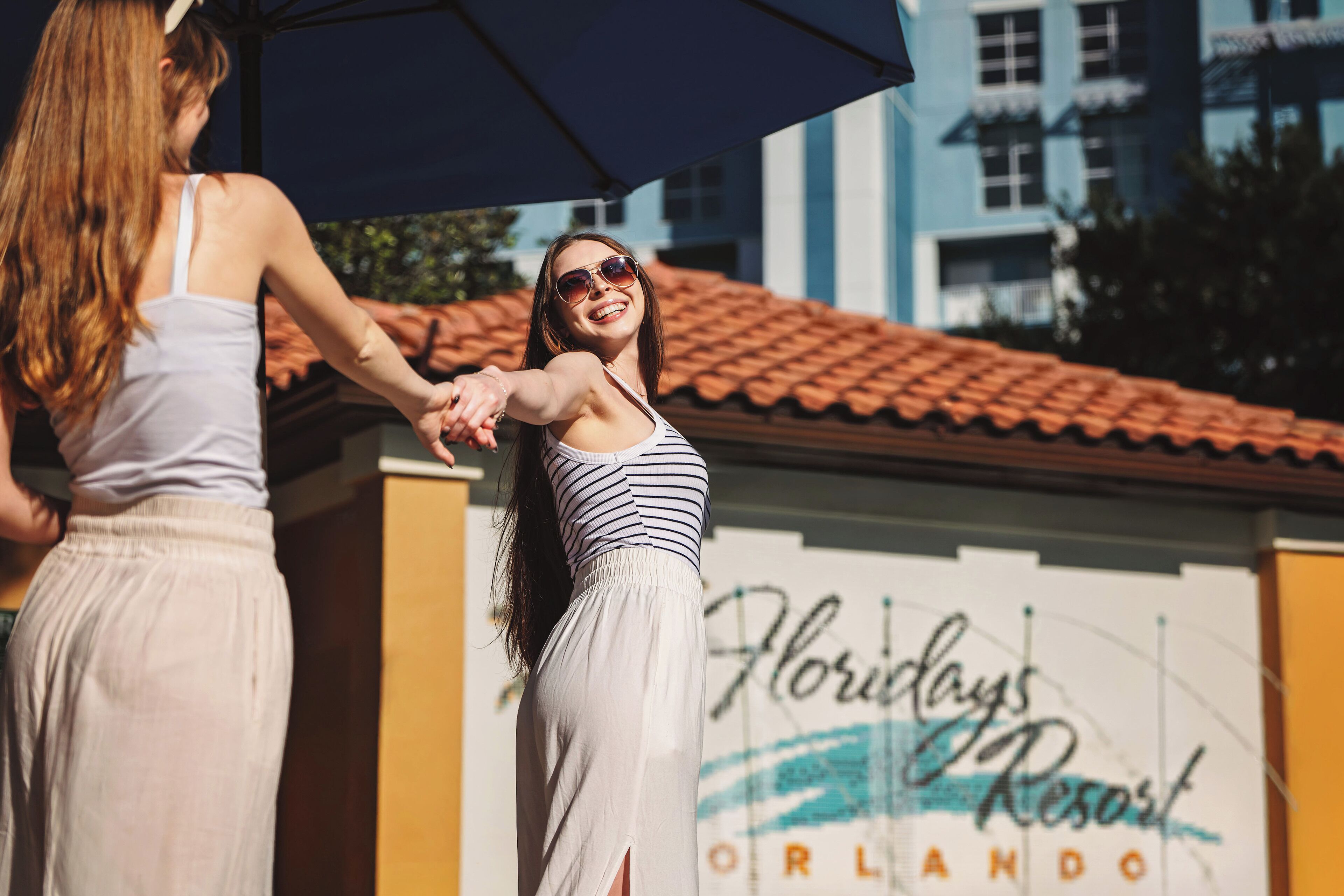 Twee personen houden elkaars hand voor een gebouw met een bord waarop staat 'Holidays Resort Orlando'.