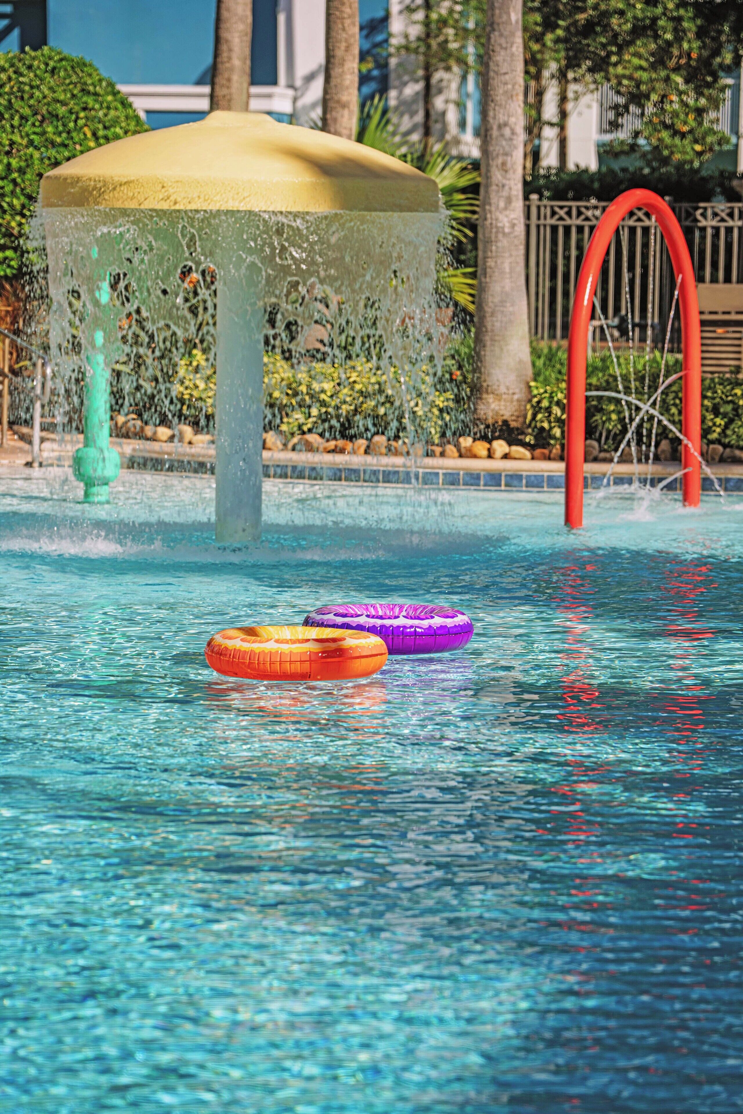 A swimming pool with a water fountain, two inflatable rings, and a red arch structure.