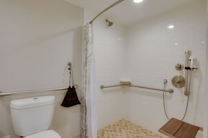 Un baño con ducha, inodoro y barra de apoyo.