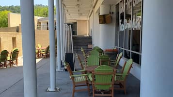 A covered outdoor seating area with green chairs and a table, a staircase leading to an upper level, and a building with a sign reading "BRINN GRILL".