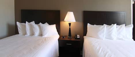 Una habitación de hotel con dos camas, una mesita de noche con lámpara y un teléfono.
