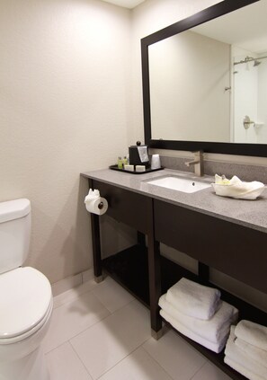 A bathroom with a white toilet, a sink with a mirror above it, and a shelf with folded towels.