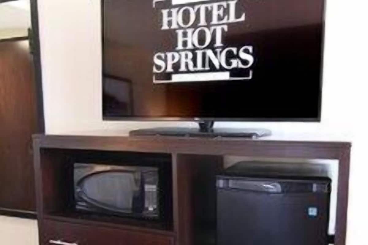 Habitación de hotel con televisión de pantalla plana sobre un mueble de madera, microondas y refrigerador.