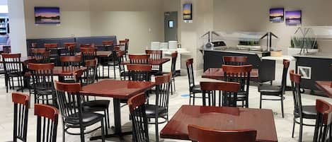 A modern restaurant with multiple dining tables and chairs, a counter with a display, and artwork on the walls.